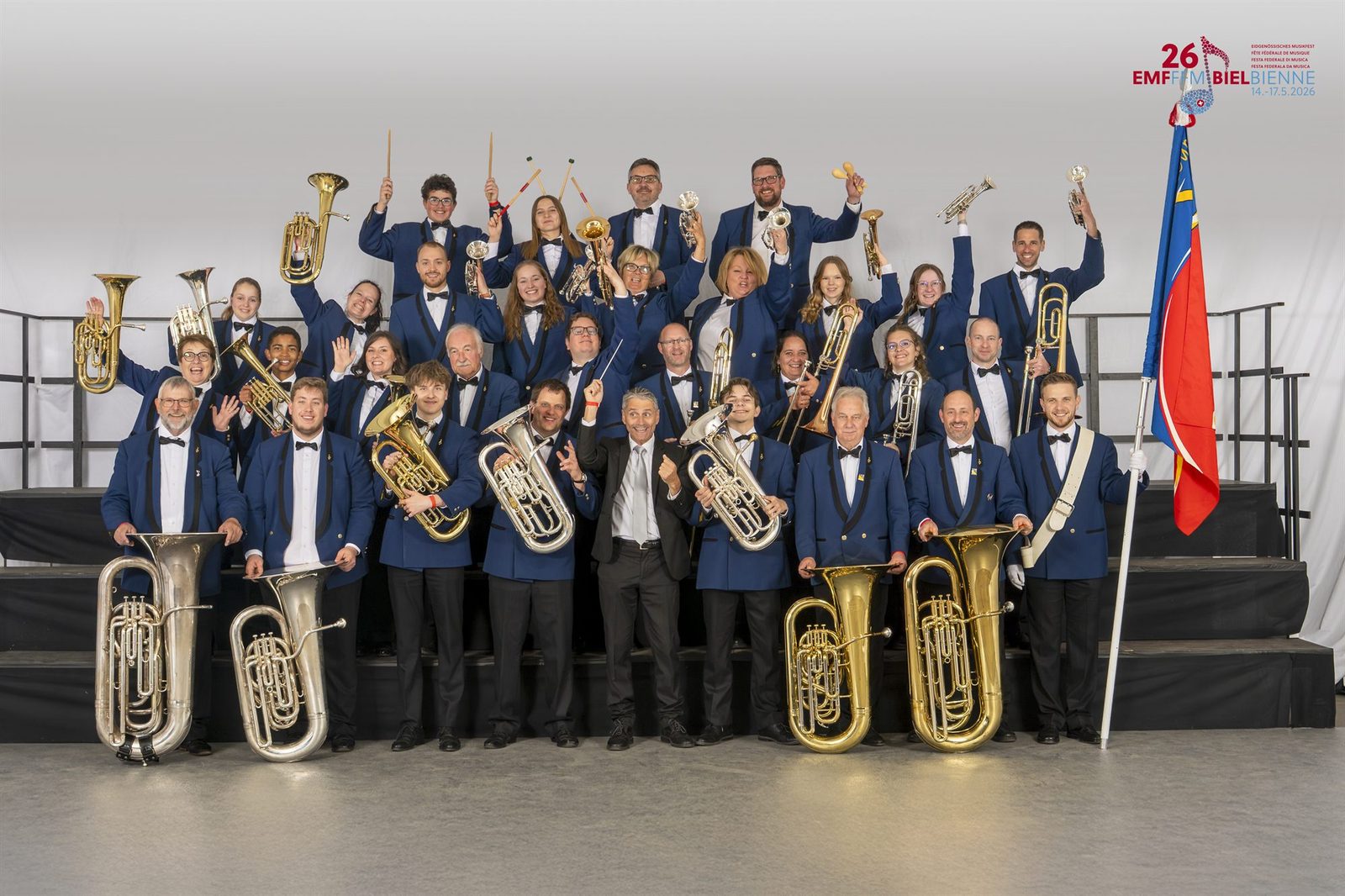 Les musiciens de l'Harmonie de Vendlincourt en veste bleue, instruments levés, autour de leur drapeau